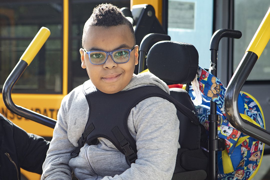Henry Viscardi Student with glasses and a wheelchair smiling in front of a school bus