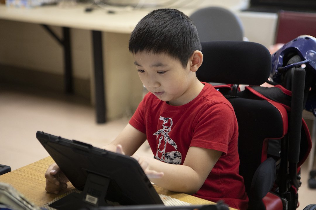 Photo of young disabled boy in a wheelchair using a laptop computer