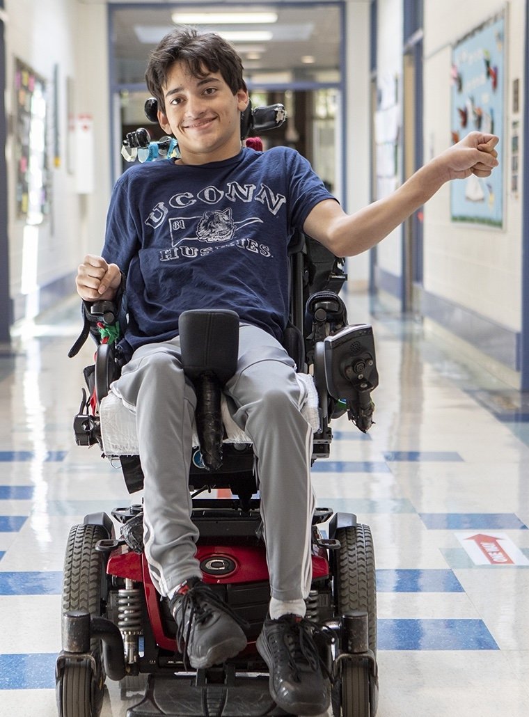 Young man in a motorized wheelchair smiling and waving